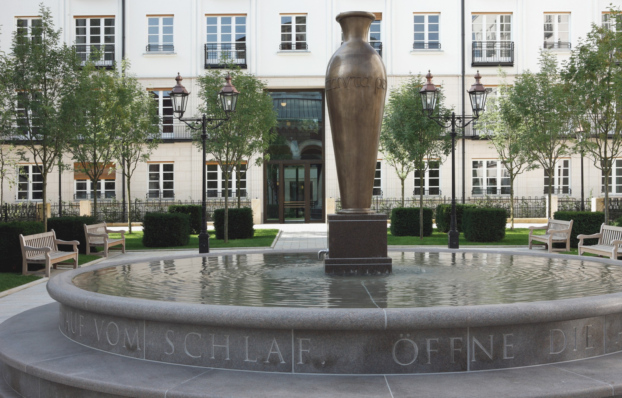 Steinbrunnen mit eingraviertem Schriftzug und zentraler Amphore im Wohnquartier Lenbach Gärten in München