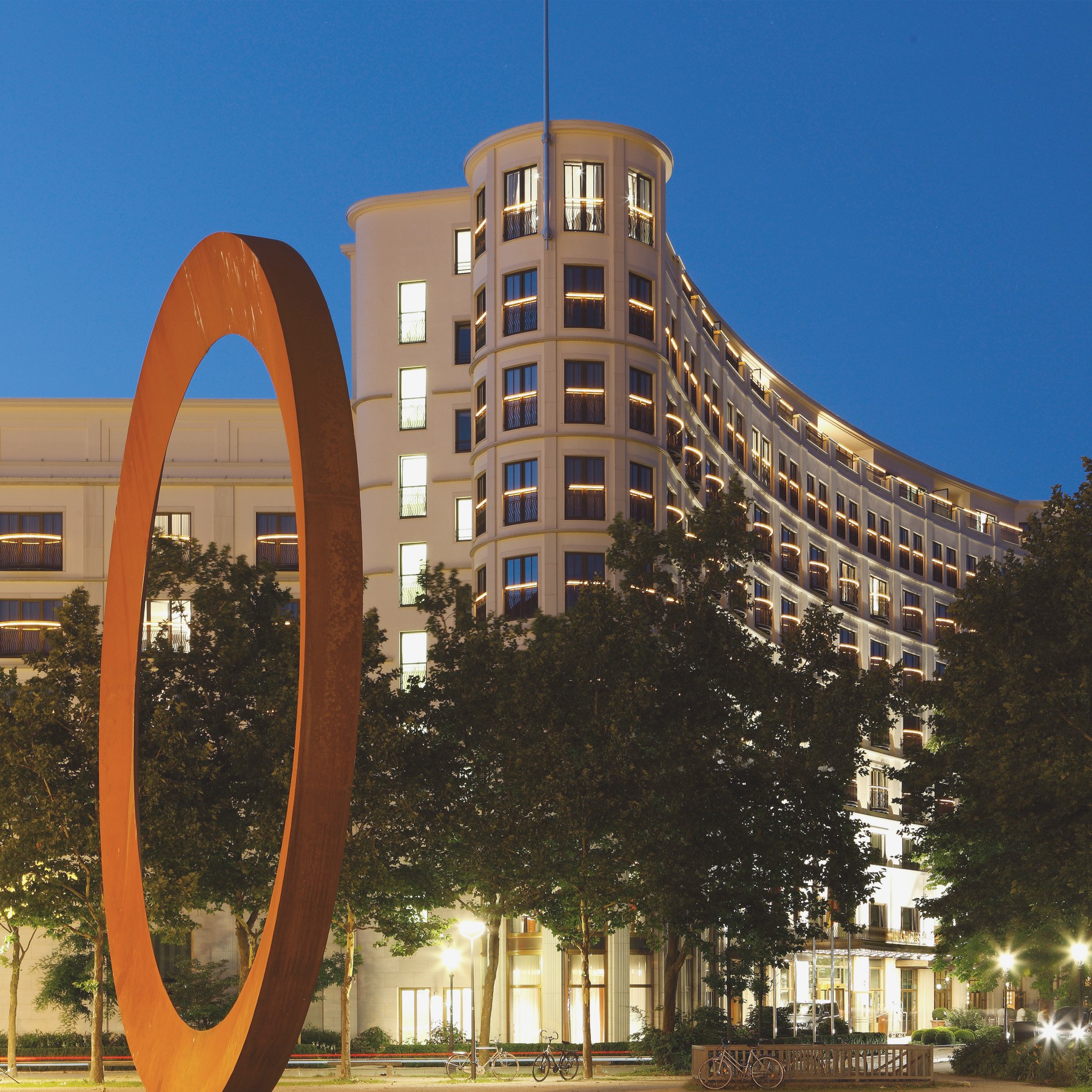 Nachts beleuchtete Fassade des Charles Hotels mit Kunstwerk im Vordergrund in den Lenbach Gärten in München