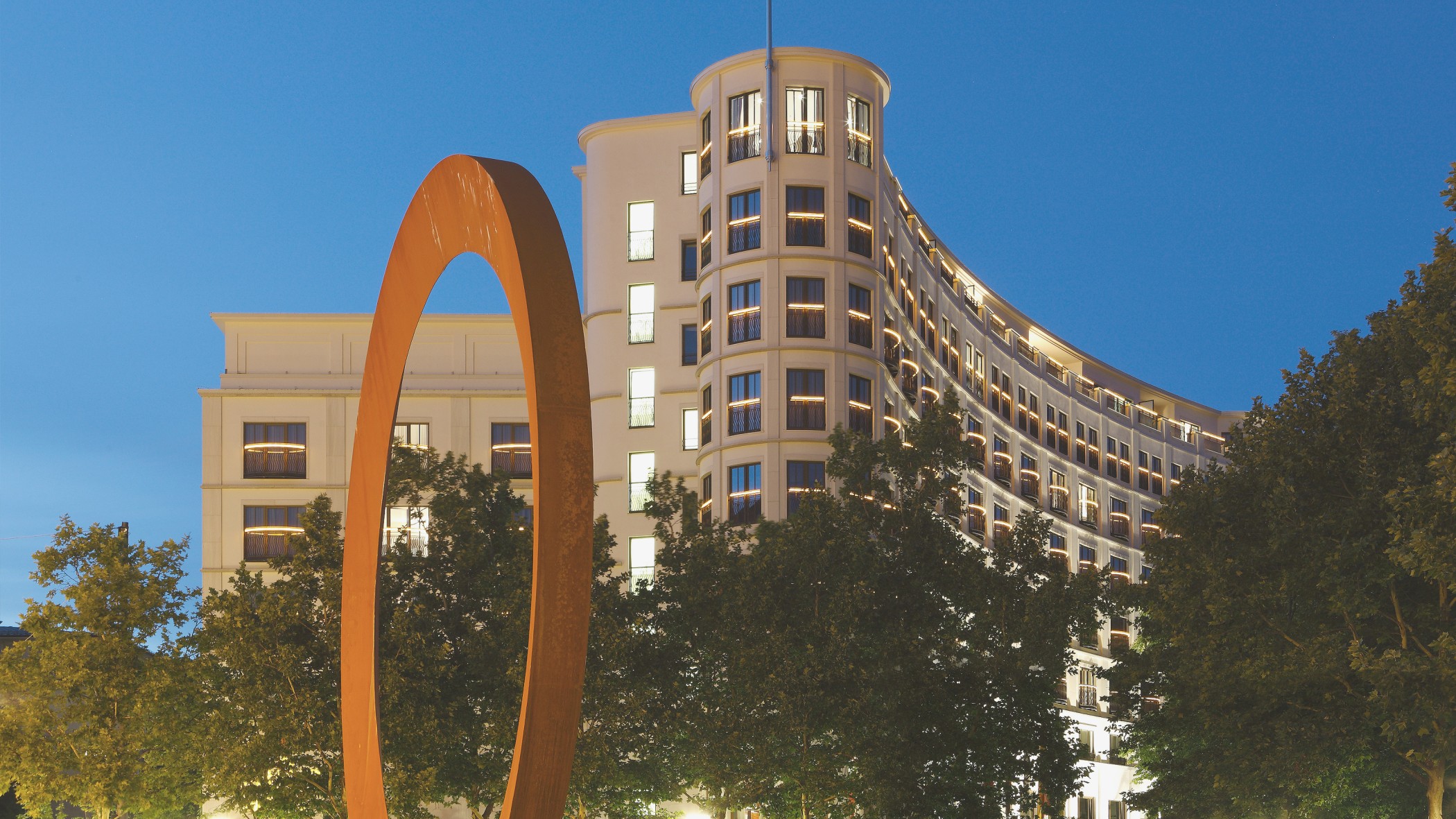 Nachts beleuchtete Fassade des Charles Hotels mit Kunstwerk im Vordergrund in den Lenbach Gärten in München