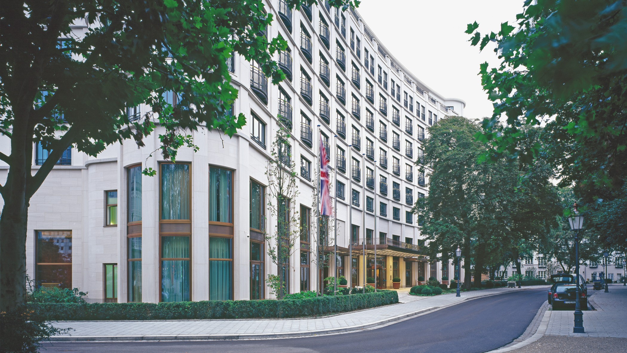 Fassade des Charles Hotels mit Bäumen und englischer Flagge in den Lenbach Gärten in München