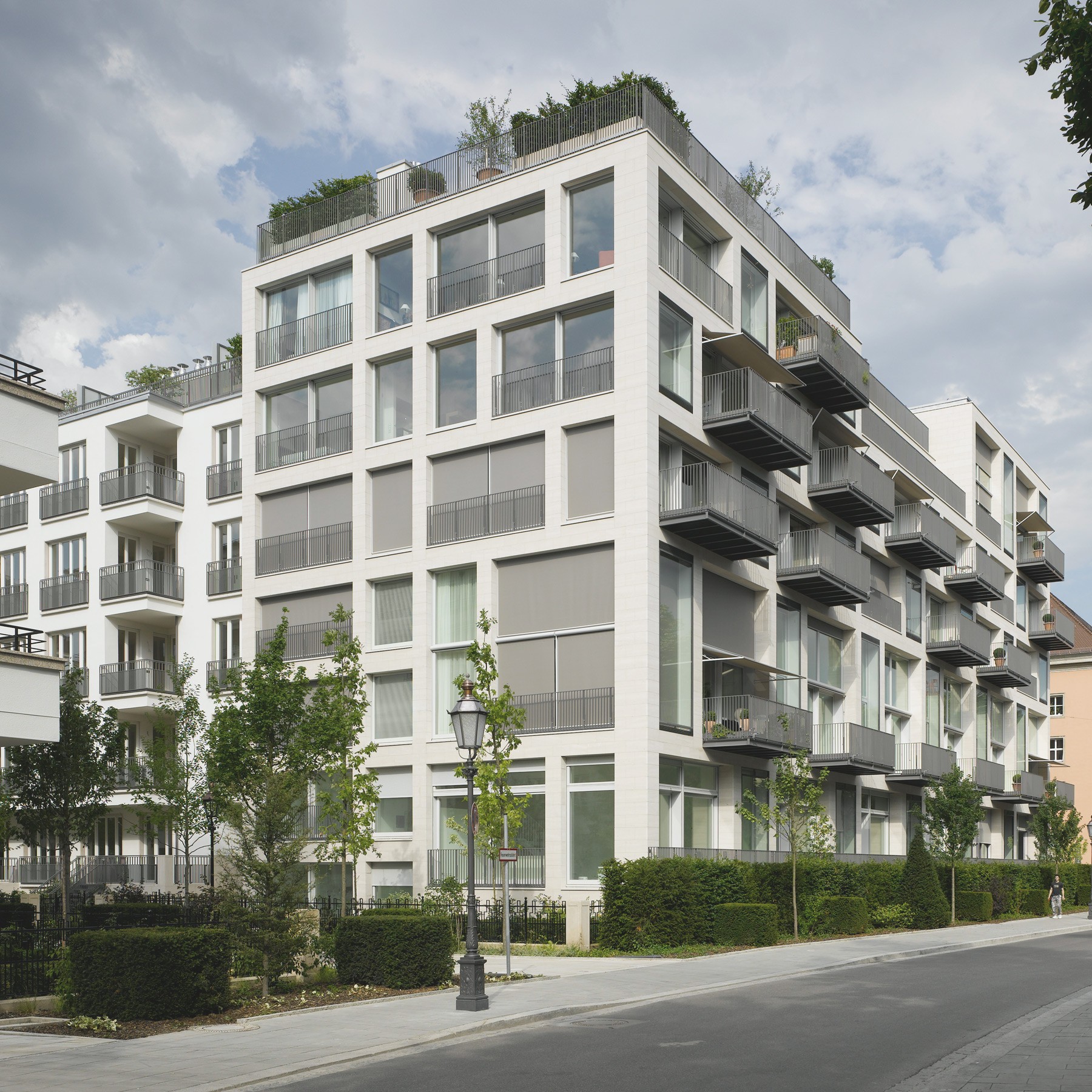 Wohngebäude mit Balkonen und grüner Parkanlage bei Sonnenschein im exklusiven Quartier Lenbach Gärten München