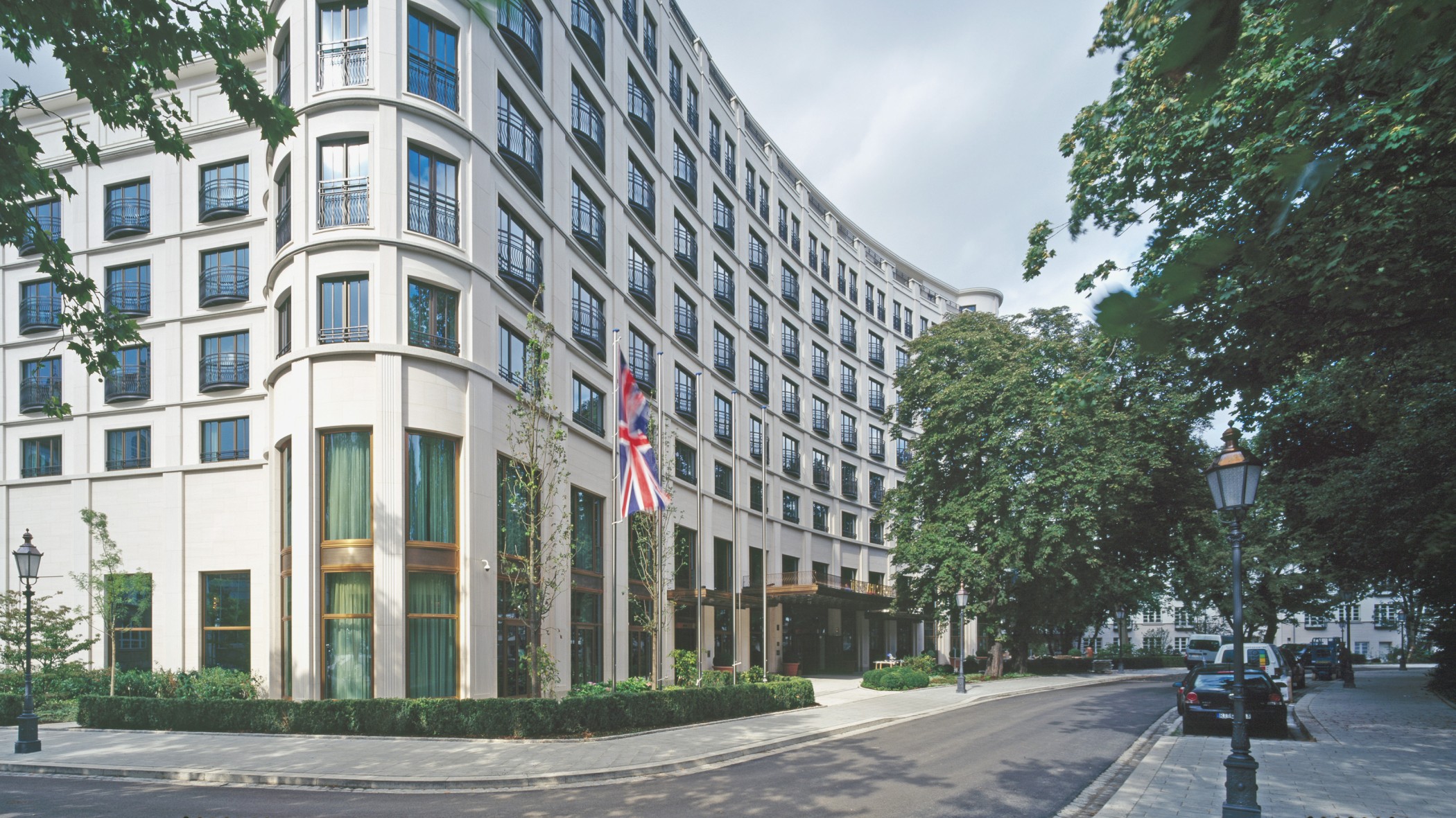 Fassade des Charles Hotels mit Bäumen und englischer Flagge im Quartier Lenbach Gärten in München