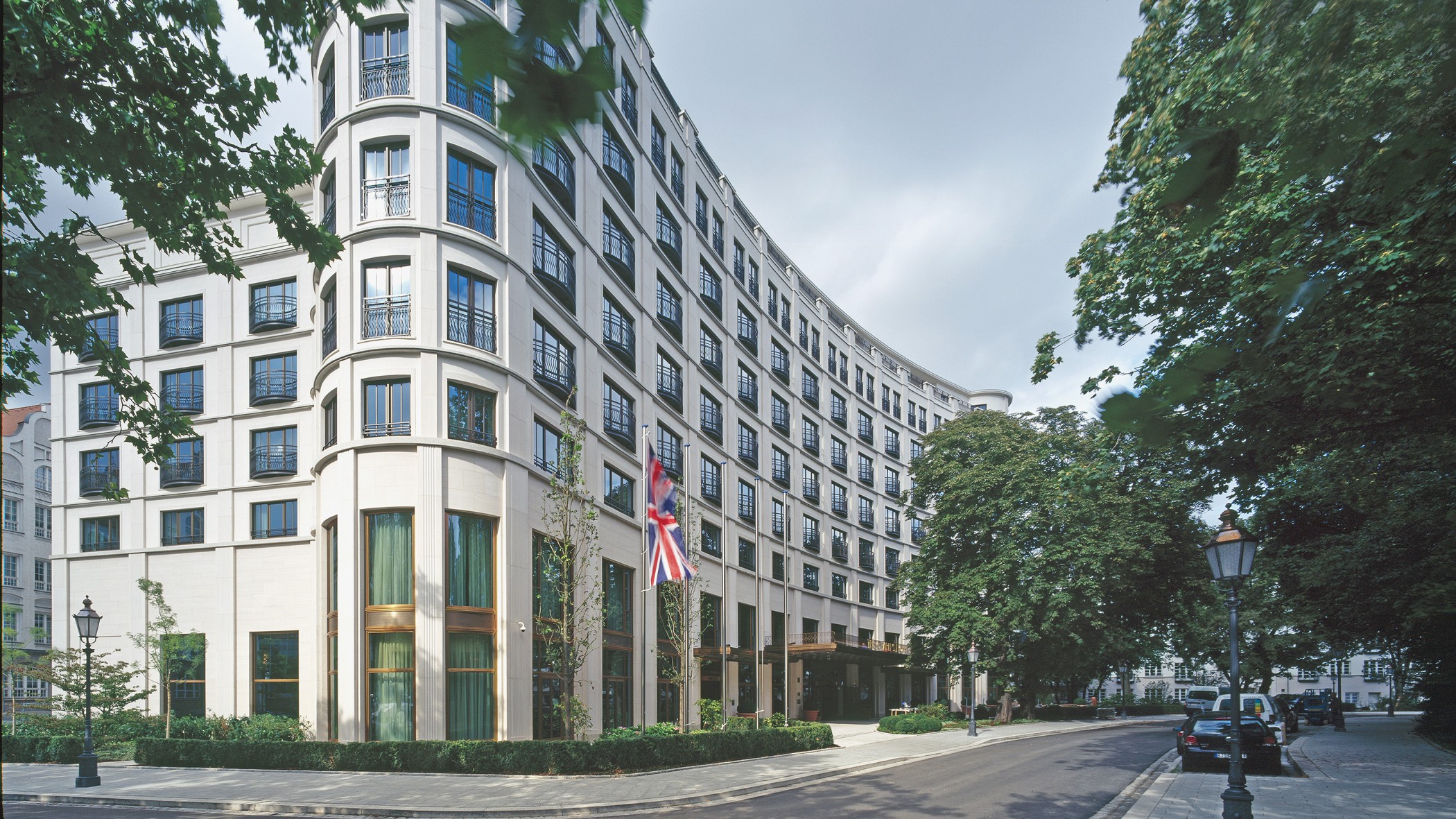 Fassade des Charles Hotels mit Bäumen und englischer Flagge in den Lenbach Gärten in München