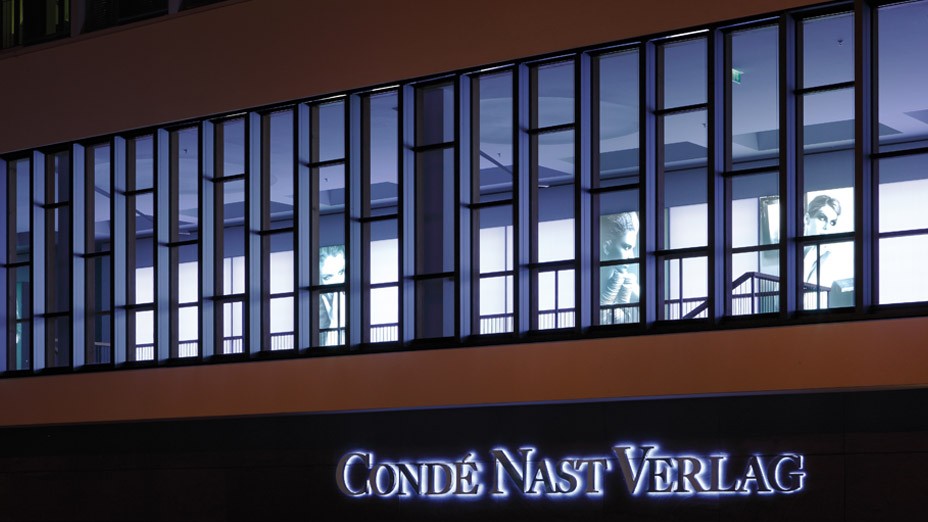 Logo des Condé Nast Verlages bei Nacht beleuchtet in den Lenbach Gärten in München