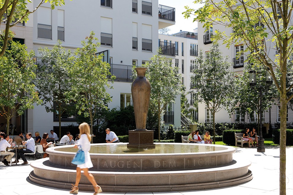 Moderne klassische Architektur mit ausblick auf den Platz mit Café und Brunnen im Wohnquartier Lenbach Gärten in München