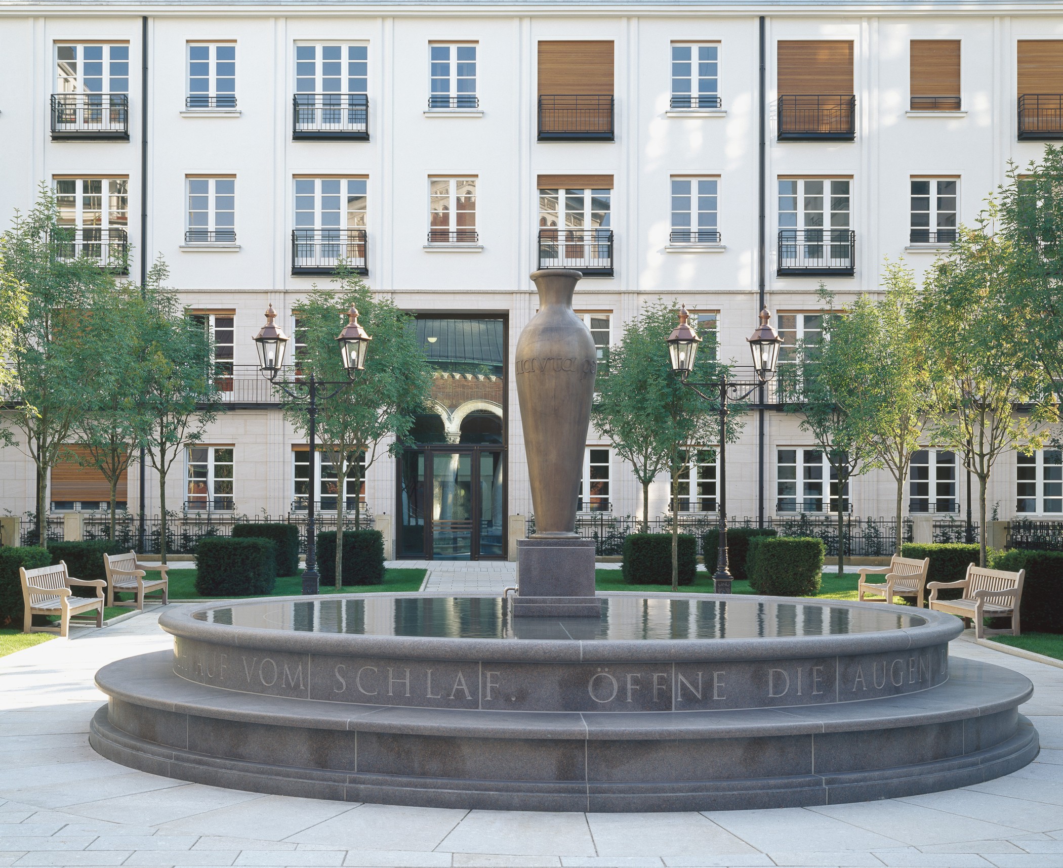 Steinbrunnen mit eingraviertem Schriftzug und zentraler Amphore im Wohnquartier Lenbach Gärten in München