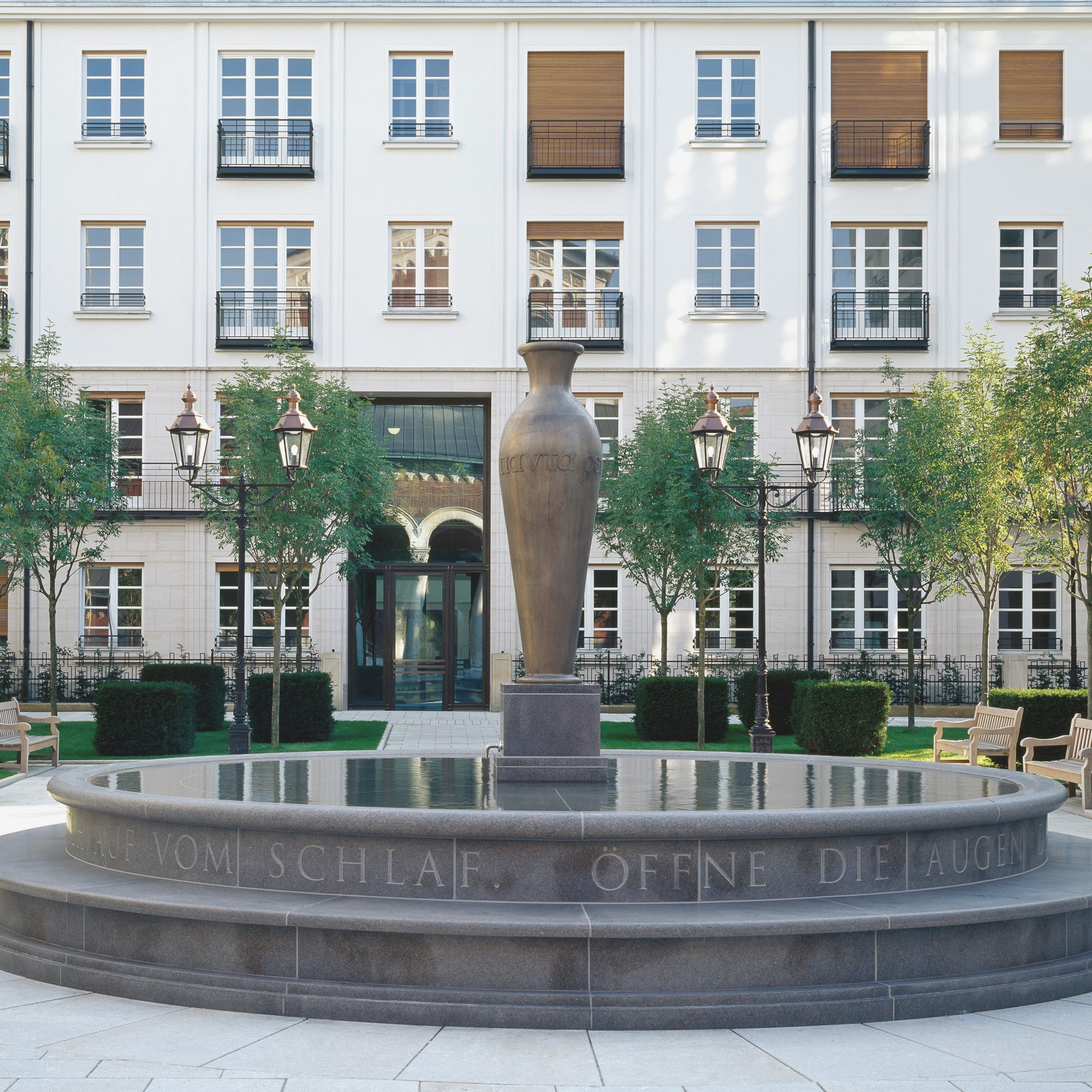 Steinbrunnen mit eingraviertem Schriftzug und zentraler Amphore im Wohnquartier Lenbach Gärten in München