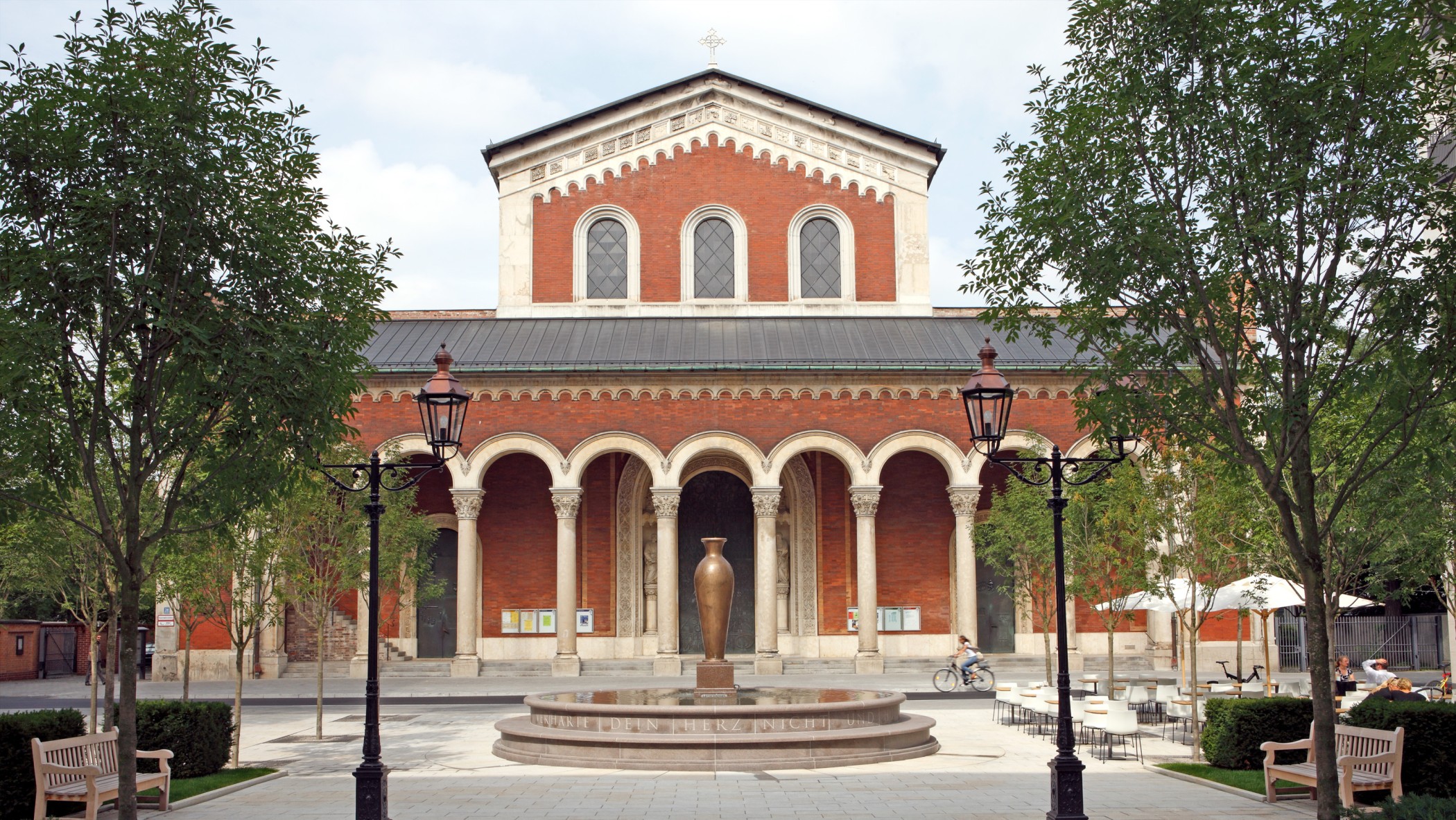 Brunnen mit Steininschrift und dekorativer Amphore vor Benediktinerabtei St. Bonifaz im exklusiven Wohnquartier Lenbach Gärten in München